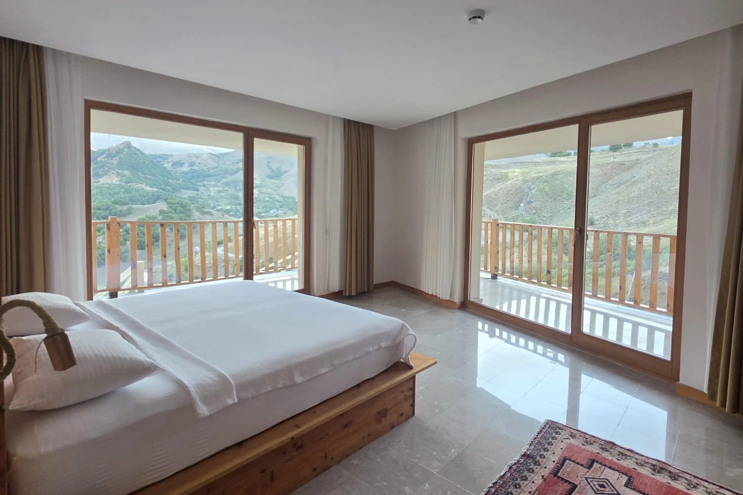 Ahşap yatak, kilim ve iki balkon kapısıyla aydınlık süit yatak odası
